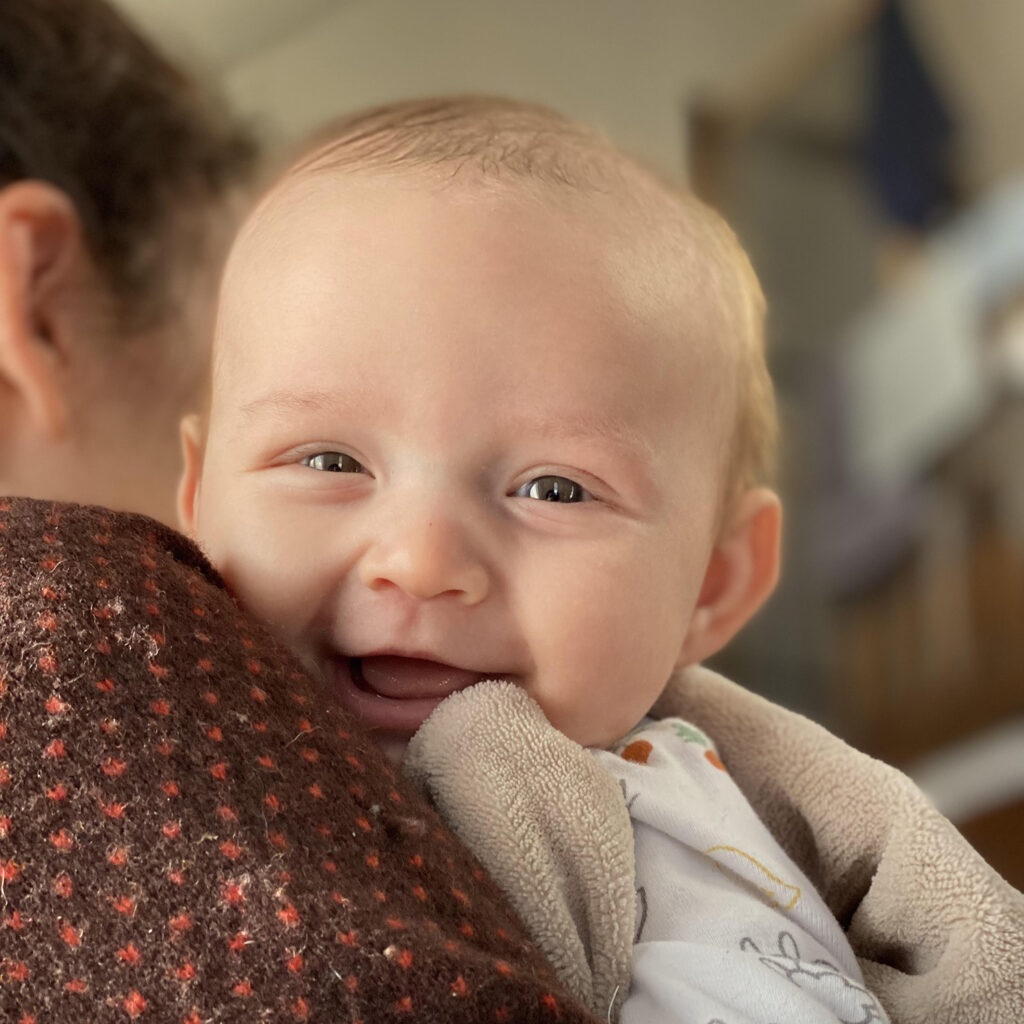 5 month old baby Smiling infant resting on a parent's shoulder, wrapped in a cozy blanket indoors.