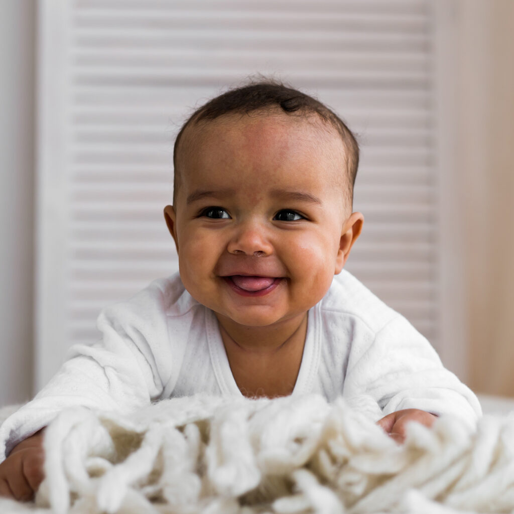 Portrait of a baby Smiling baby lying on a bed with a cozy blanket, wearing a white onesie.