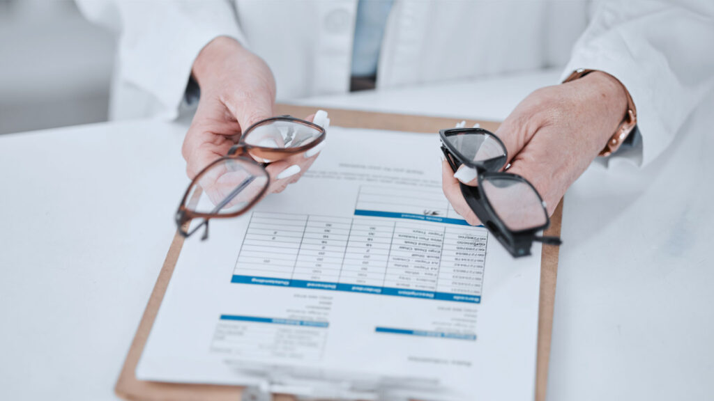 Optometrist holding eyeglasses options over a clipboard with vision test results.