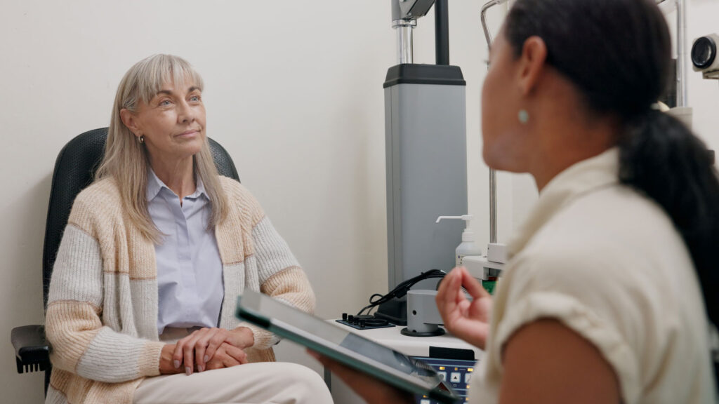 Elderly woman having an eye exam consultation with a healthcare professional in a medical office setting.