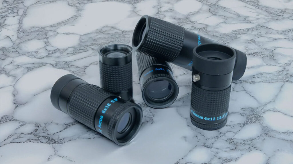 Stacked black monocular lenses on a white marbled surface, featuring various magnifications.