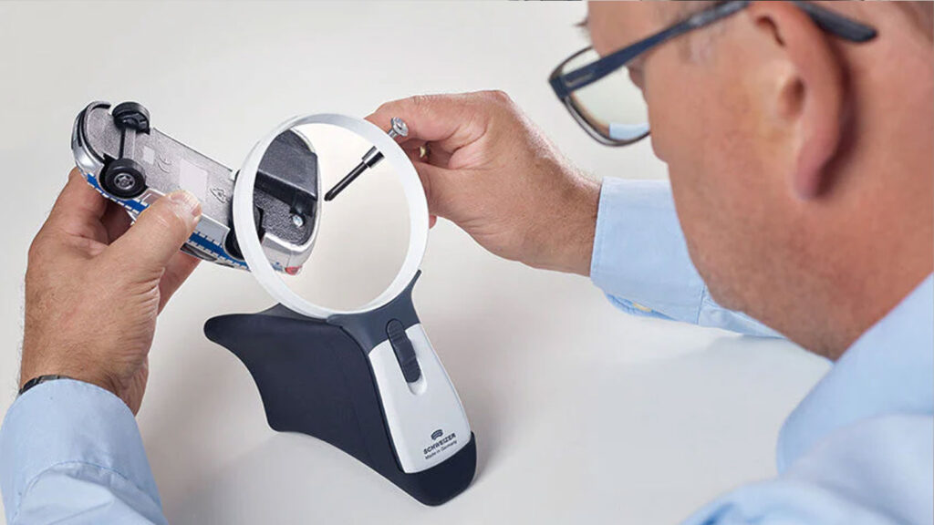 Man uses magnifier to examine toy car details closely with precision tool.