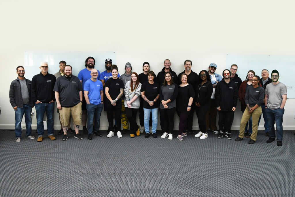 Chadwick Optical Family (Employee) Photo Team standing together in an office setting, smiling for a group photo, diverse and casual atmosphere.