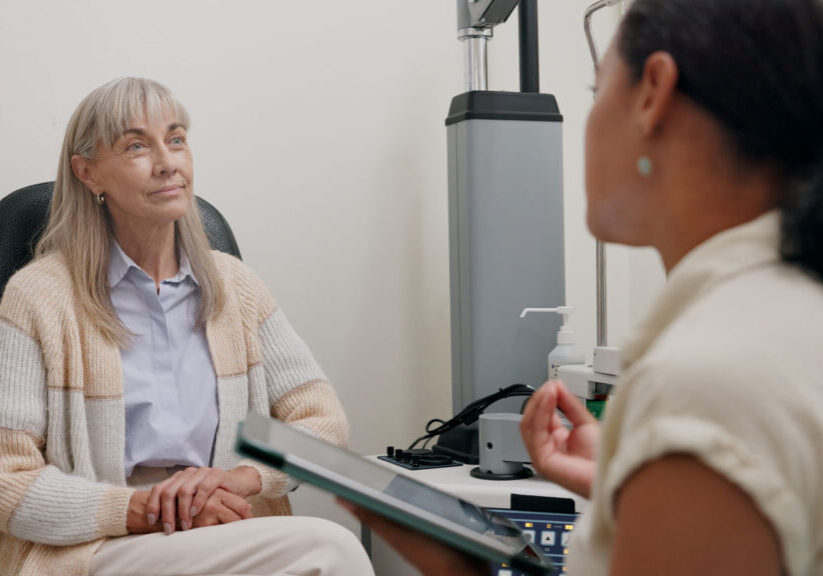 Elderly woman having an eye exam consultation with a healthcare professional in a medical office setting.