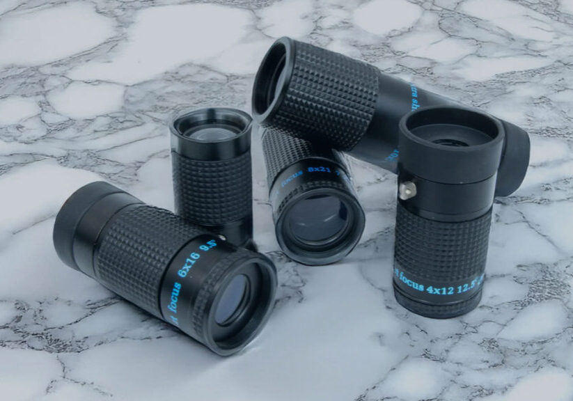 Stacked black monocular lenses on a white marbled surface, featuring various magnifications.