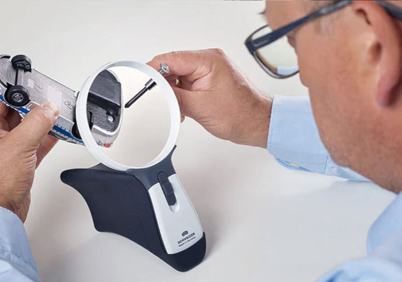 Man uses magnifier to examine toy car details closely with precision tool.
